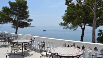 Terraza con mobiliario al aire libre que da a un mar tranquilo, con árboles y una isla distante a la vista.