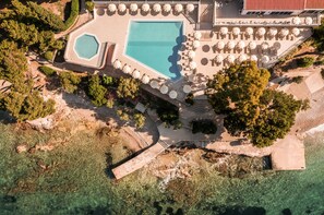 An aerial view of a resort with a large swimming pool, sun loungers, and a beach area.