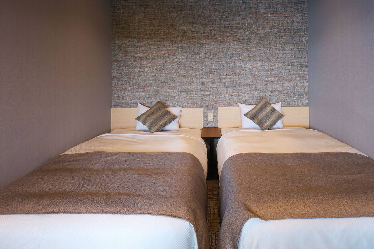 A double bed with a headboard, two pillows, and a brown throw blanket.