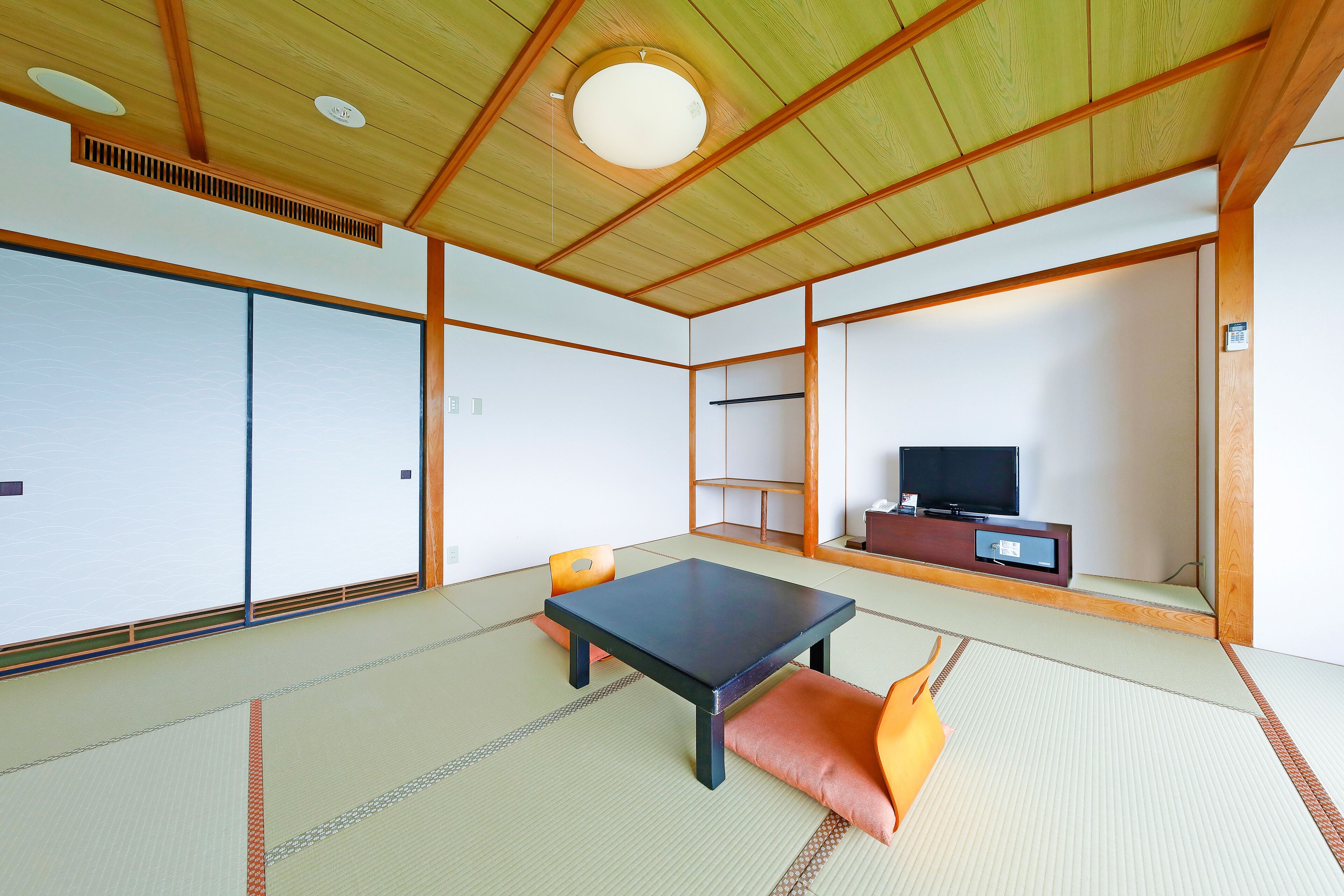 Una habitación tradicional japonesa con suelo de tatami, una mesa baja, cojines y un televisor sobre un mueble de madera.