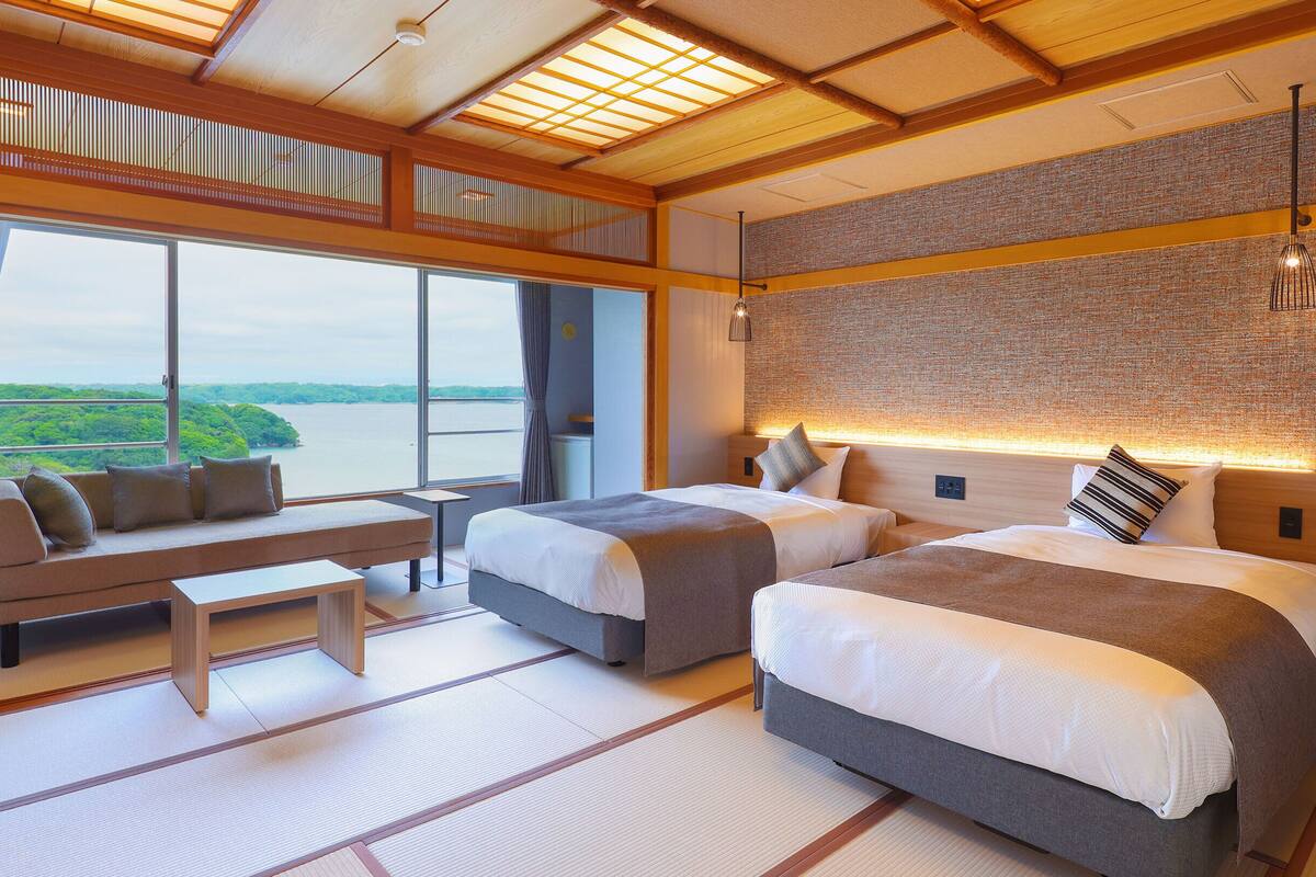 A hotel room with two beds, a sofa, a small table, and a view of a body of water.
