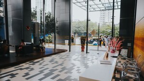 Un hall d’hôtel moderne avec un sol à motifs géométriques, des portes en verre transparent et un comptoir d’accueil doté de chaises.
