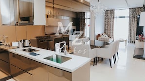 Une cuisine moderne dotée d’un îlot central, d’un coin repas avec des meubles blancs et d’un grand miroir qui agrandit visuellement l’espace.