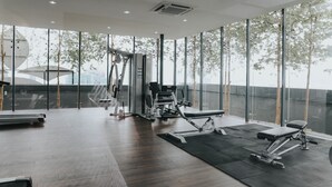 Une salle de sport moderne, équipée de mat ériel d’exercice, dotée de grandes fenêtres et offrant une vue sur les arbres et les bâtiments.