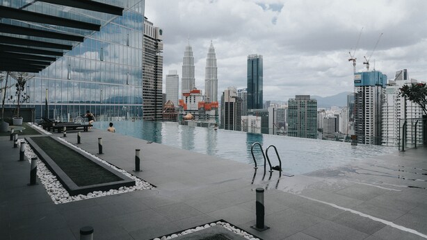 Une piscine sur le toit offrant une vue sur les tours Petronas, entourée d’immeubles modernes.