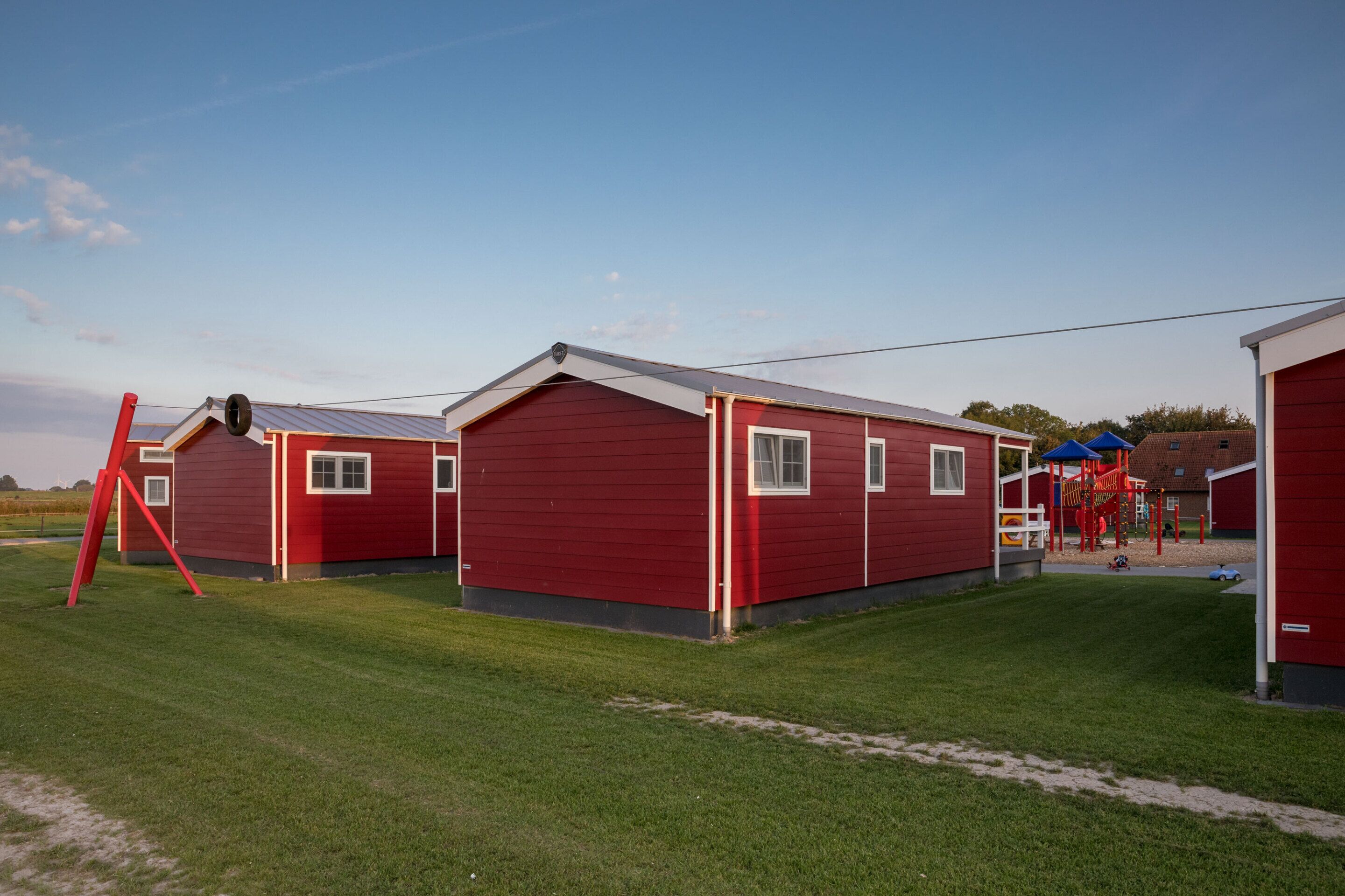 Eine Reihe roter Holzhütten mit einem Spielplatz im Hintergrund.