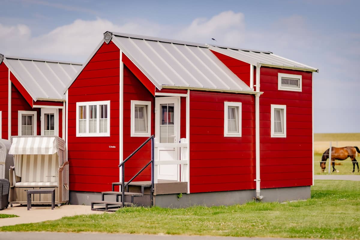 A red building with white trim, a covered outdoor seating area, and a horse in the background.