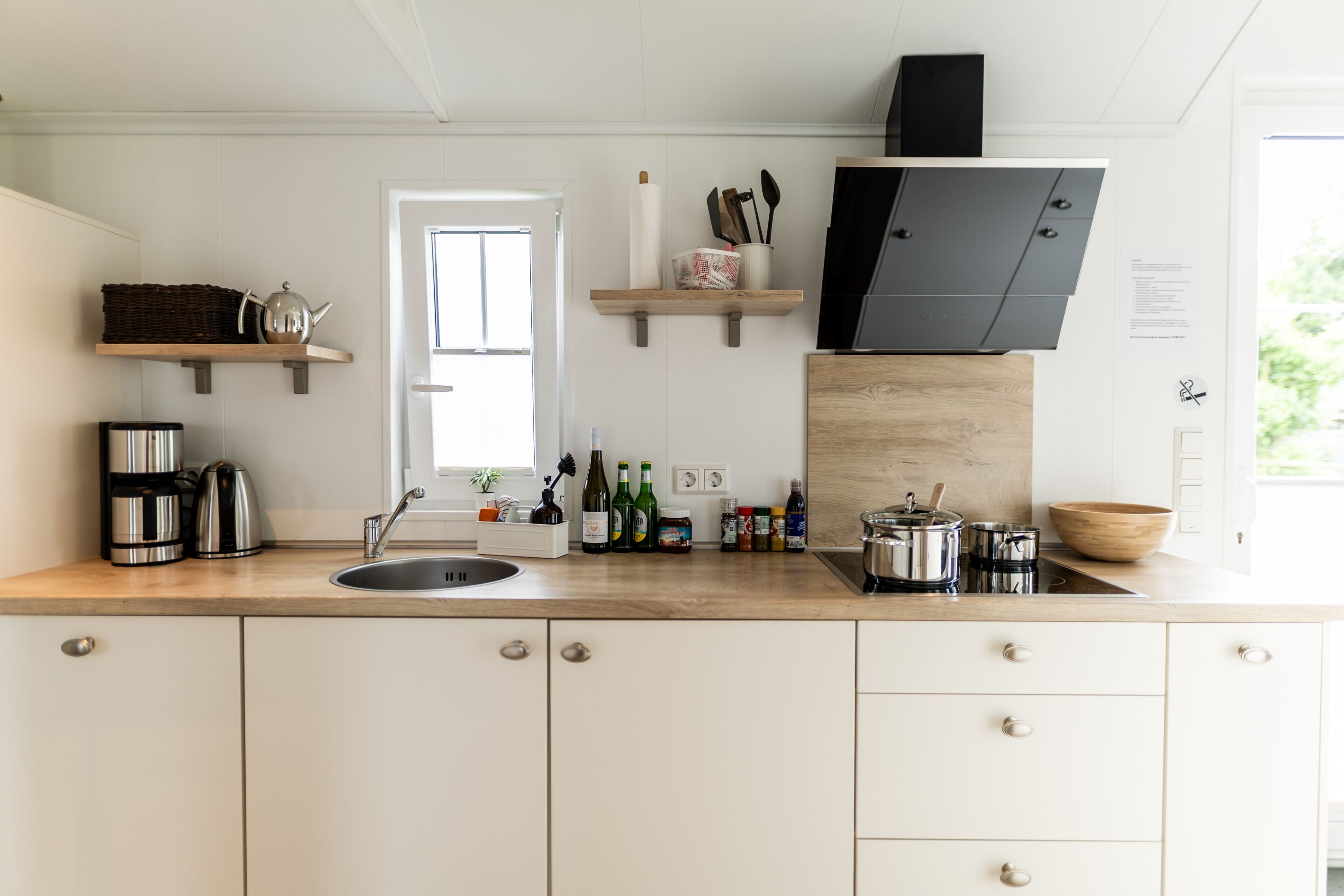 A modern kitchen with white cabinets, a wooden countertop, a built-in stove, and various kitchen appliances and utensils.