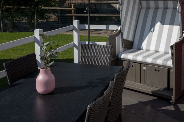 An outdoor patio with a black table, wicker chairs, a striped sofa, and a pink vase with plants. - Ferienhof Schild (Wangerland)