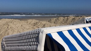 A beach view with a striped beach chair and a rocky shoreline. - Ferienhof Schild (Wangerland)