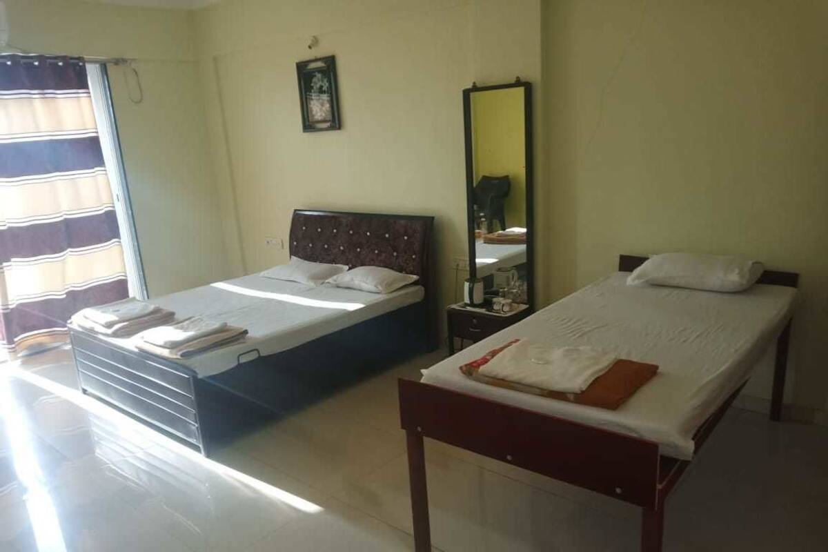 A room with two single beds, a bedside table with a lamp, a window with curtains, and a wall-mounted mirror.