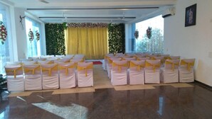 A room with rows of chairs arranged for an event, a stage with a curtain, and decorative wall hangings. - Dreammland Resort (Shahapur)