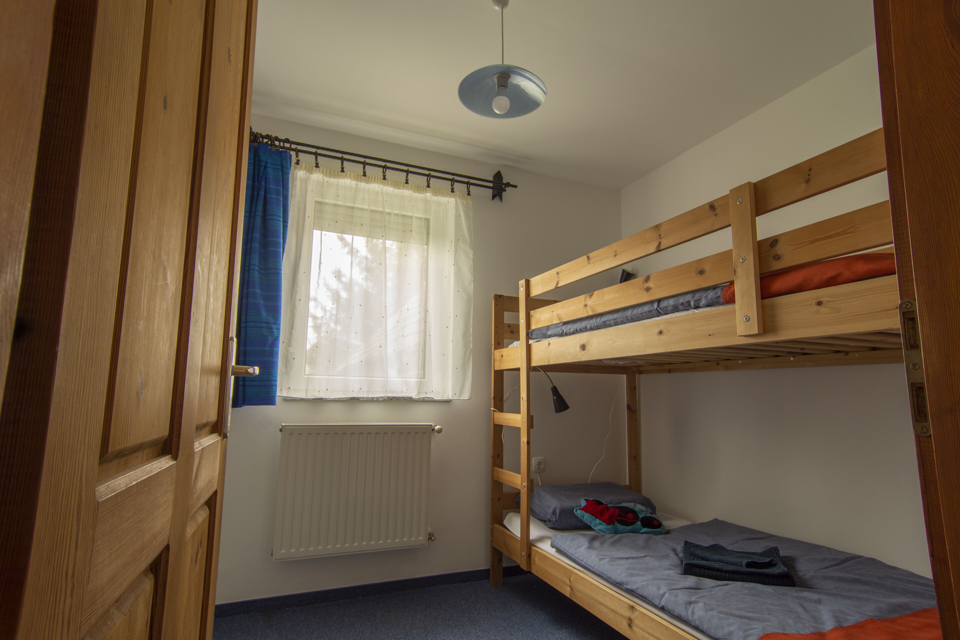 A room with a bunk bed, a window with curtains, a radiator, and a ceiling light.