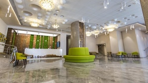 Een moderne lobby met een receptiebalie, groene zitplaatsen en een kroonluchter.