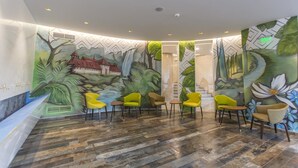 Een hal met een muurschildering van een waterval en begroeiing, houten vloeren en gele stoelen.