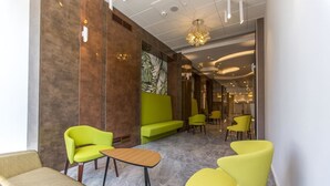 Een moderne lobby met felle gele stoelen, een groene bank en een marmeren vloer.