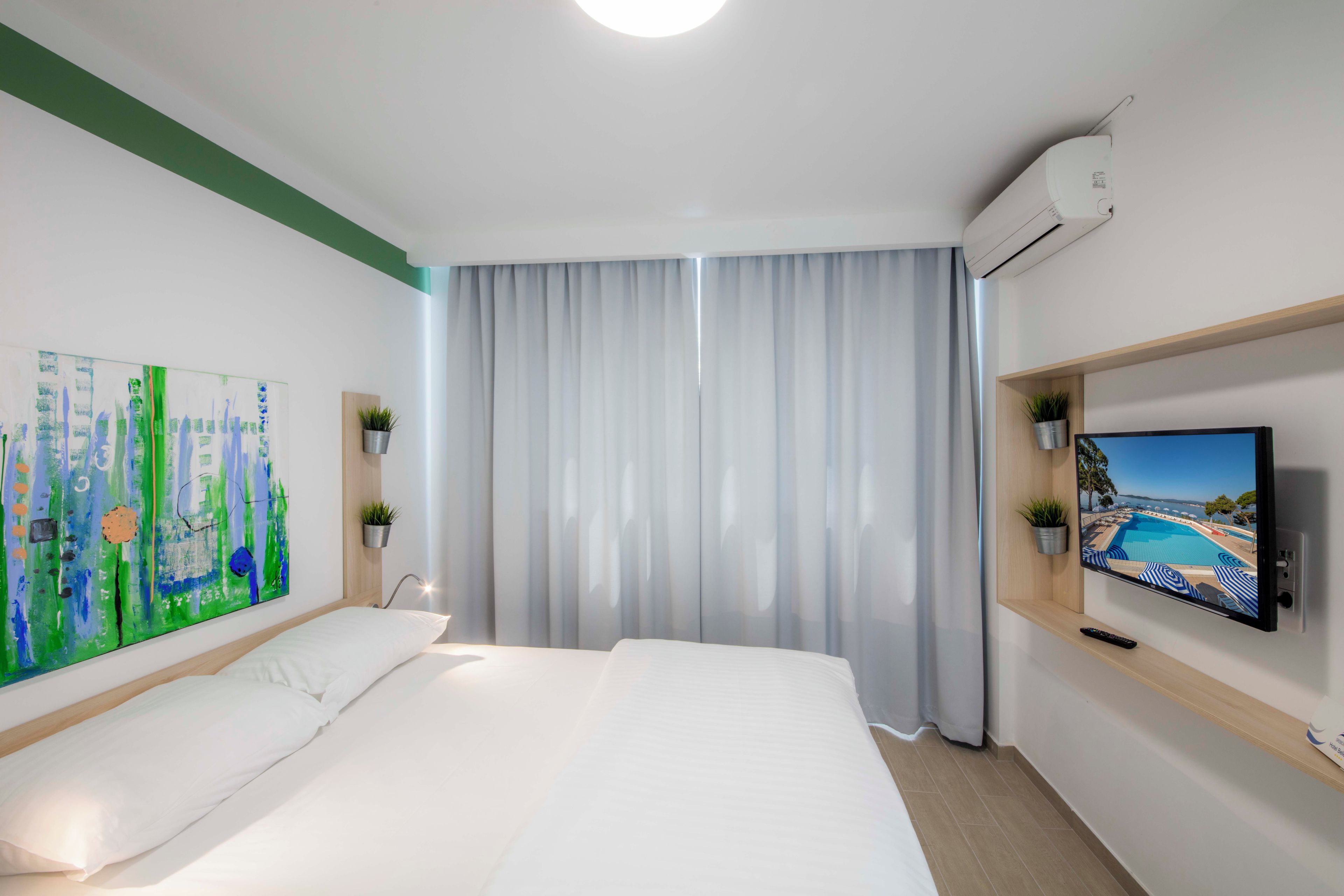 A hotel room with a large bed, a painting on the wall, a television, and a window with curtains.
