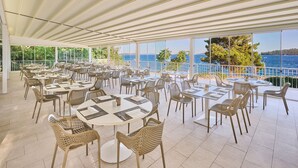 A spacious outdoor dining area with multiple tables and wicker chairs, overlooking a scenic coastline. - Bellevue Maradiso Casa by Aminess (Orebic)