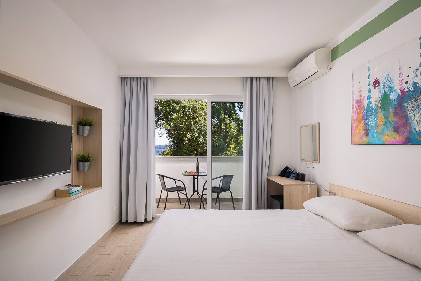 Habitación de hotel con cama, escritorio, silla, televisor y ventana con cortinas.