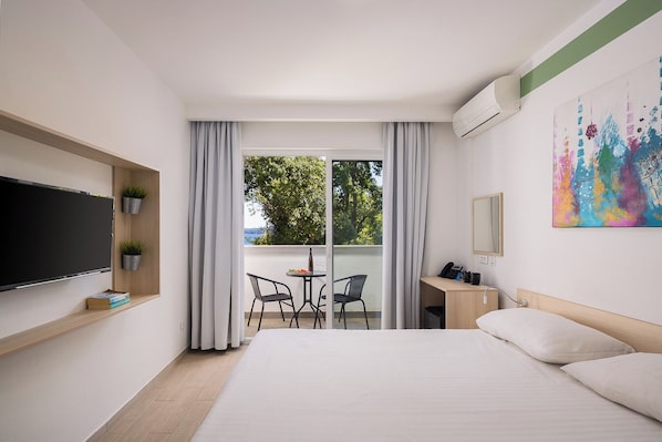 Habitación de hotel con cama, escritorio, silla, televisor y ventana con cortinas.