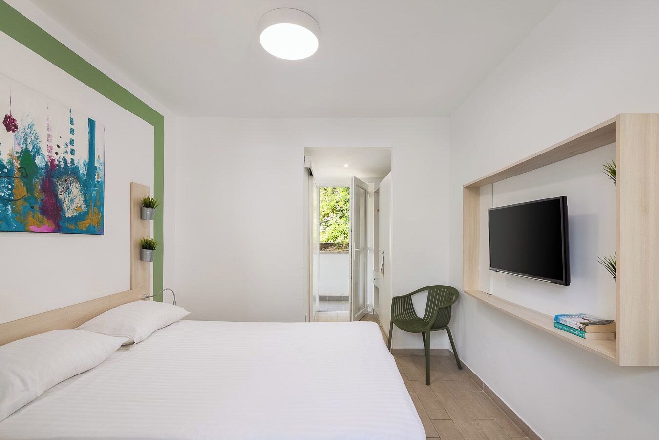 Een moderne slaapkamer met een bed, een aan de muur bevestigde televisie en een schilderij.