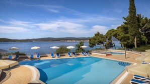 A pool with blue water, surrounded by lounge chairs and umbrellas, with a view of the sea and hills in the background. - Bellevue Maradiso Casa by Aminess (Orebic)