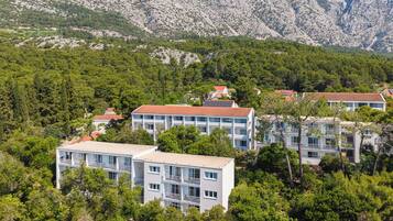 A cluster of multi-story buildings with balconies, surrounded by dense greenery and mountains in the background.