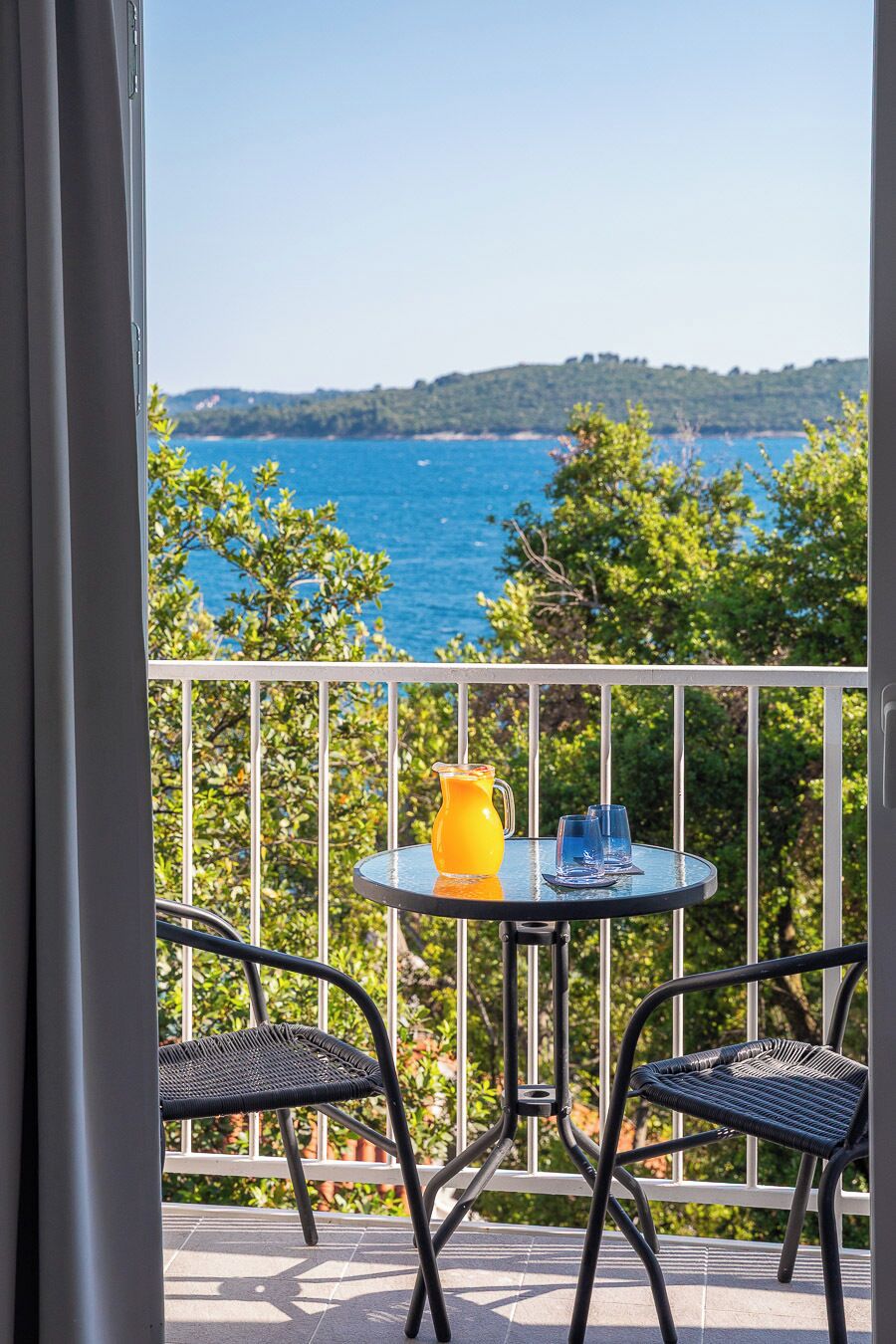 A balcony with a table and chairs, overlooking a body of water and greenery.