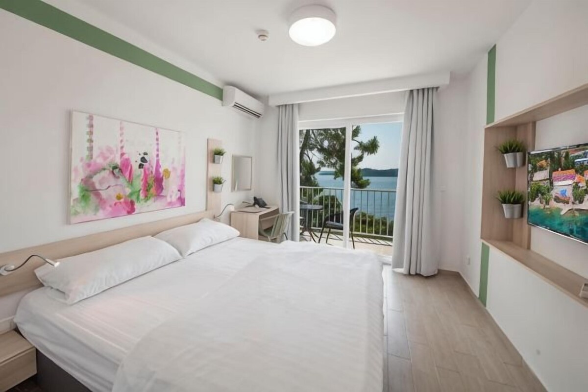 Habitación de hotel con cama, escritorio, silla, televisor y balcón con vistas.