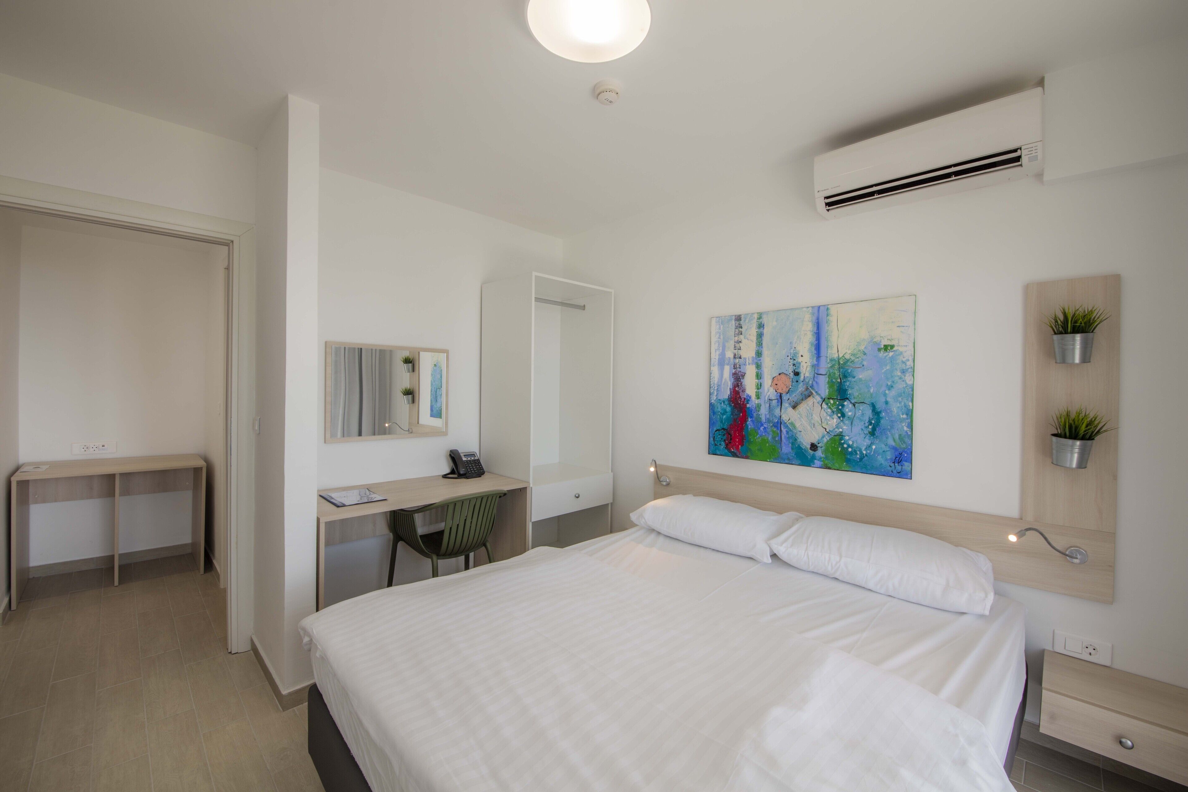 Een hotelkamer met een bed, bureau, stoel en een schilderij aan de muur.