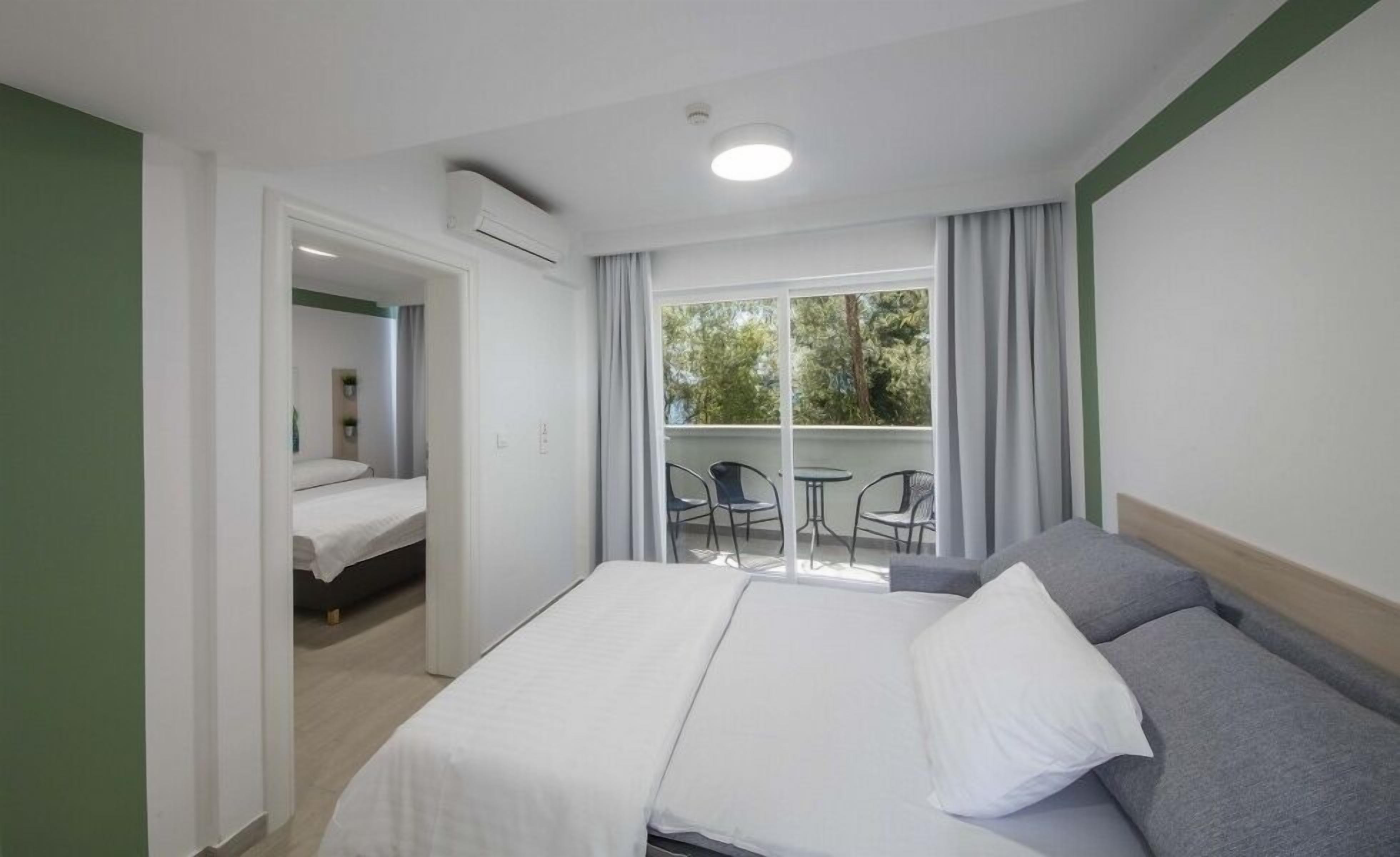 Una camera d'albergo con un letto, un balcone con sedie e vista sugli alberi.