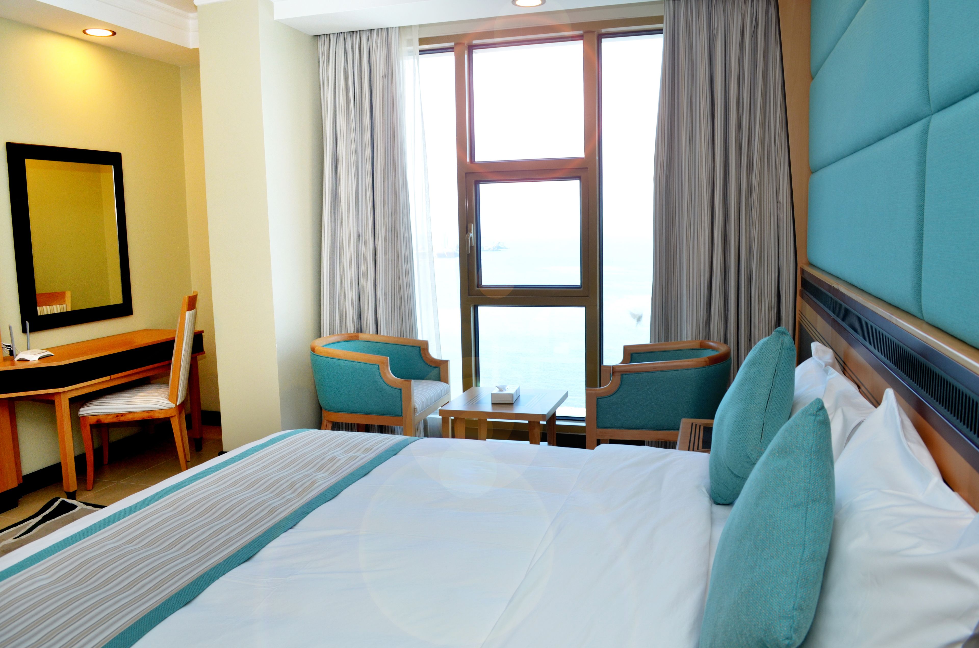 Habitación de hotel con una cama grande, dos sillas, un escritorio y una ventana con cortinas.