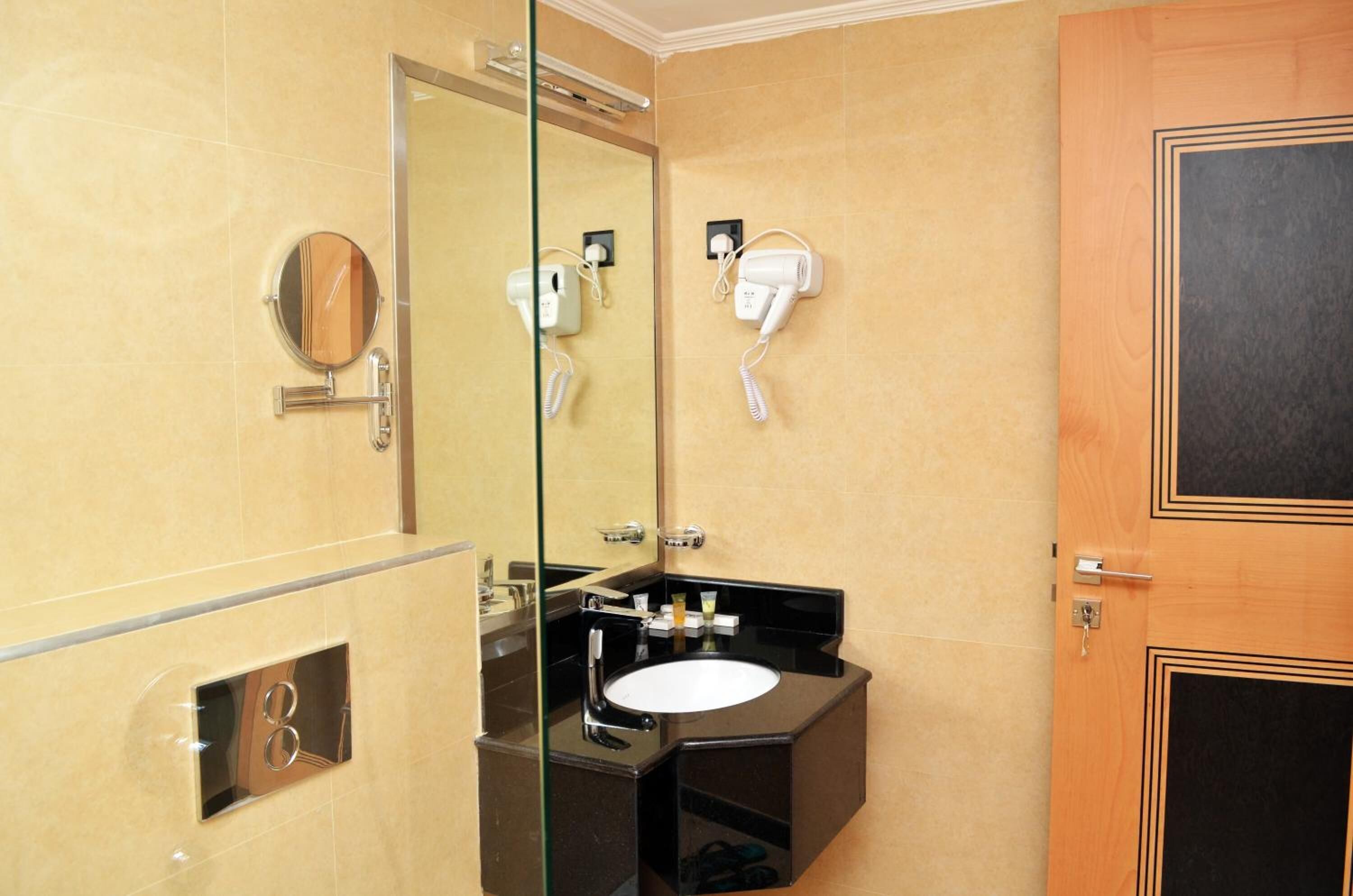 Une salle de bain avec un lavabo noir, un miroir et deux sèche-cheveux fixés au mur.