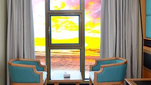 A room with two chairs, a small table, and a view of a sunset through a window with multiple panes. - Nooh Tower (Hidd)