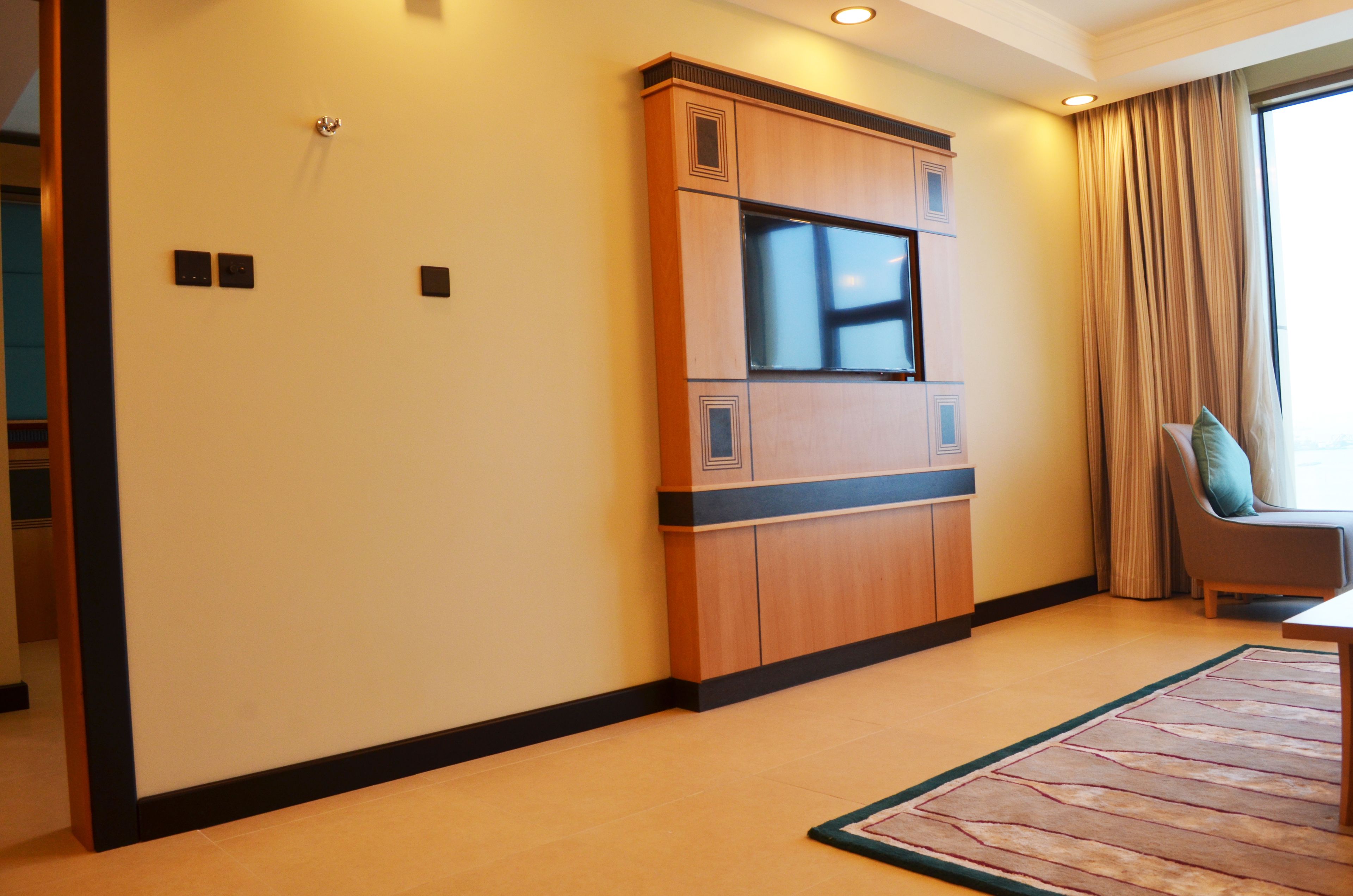 A hotel room with a built-in TV, a sofa, and a large window with curtains.