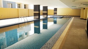 An indoor swimming pool with clear water, tiled floor, and a tiled deck area. - Nooh Tower (Hidd)
