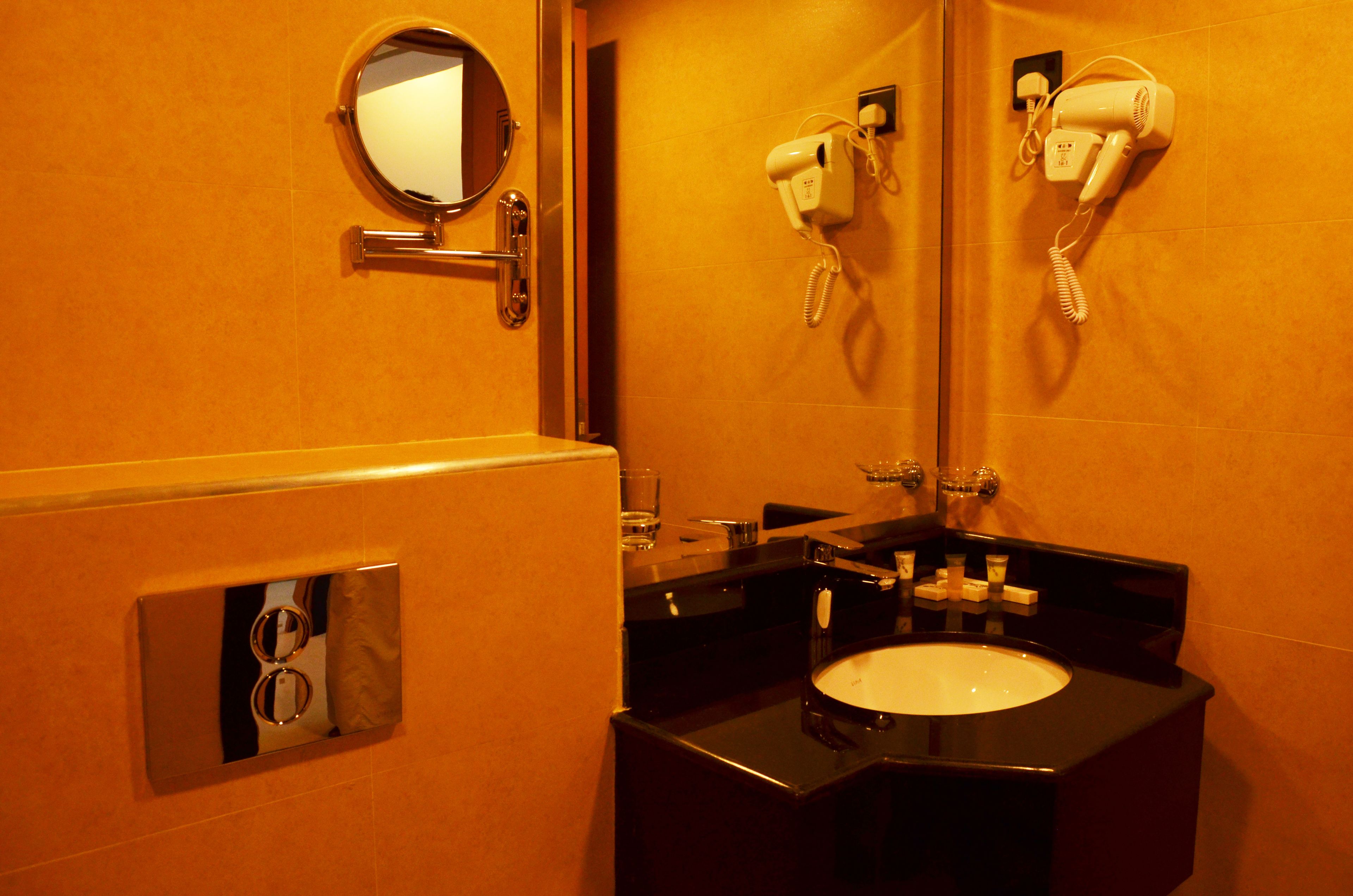 A bathroom with a round mirror, a hairdryer, and a sink.