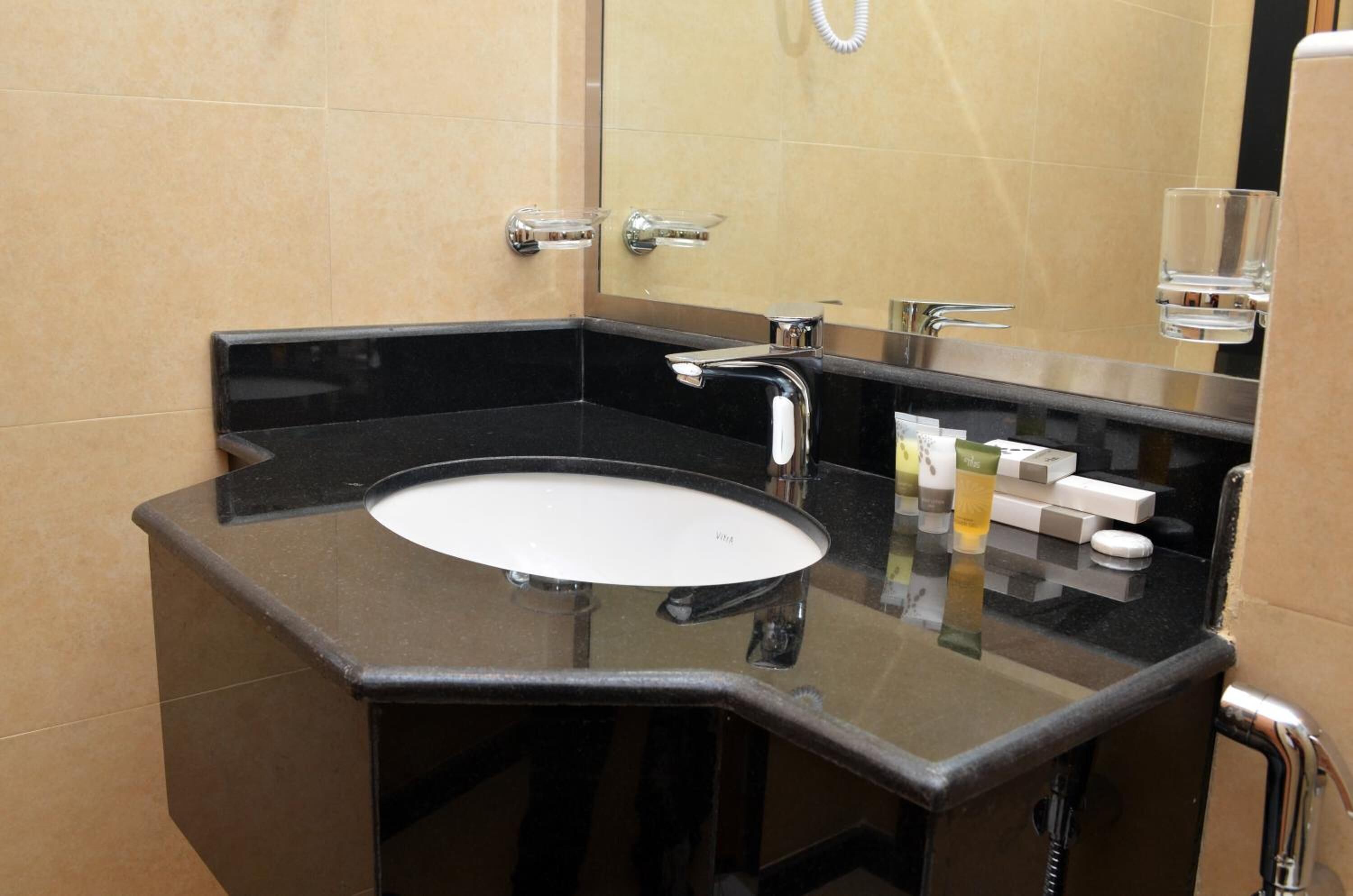 Un baño moderno con lavamanos de superficie negra, grifería cromada y dispensador de jabón de vidrio.
