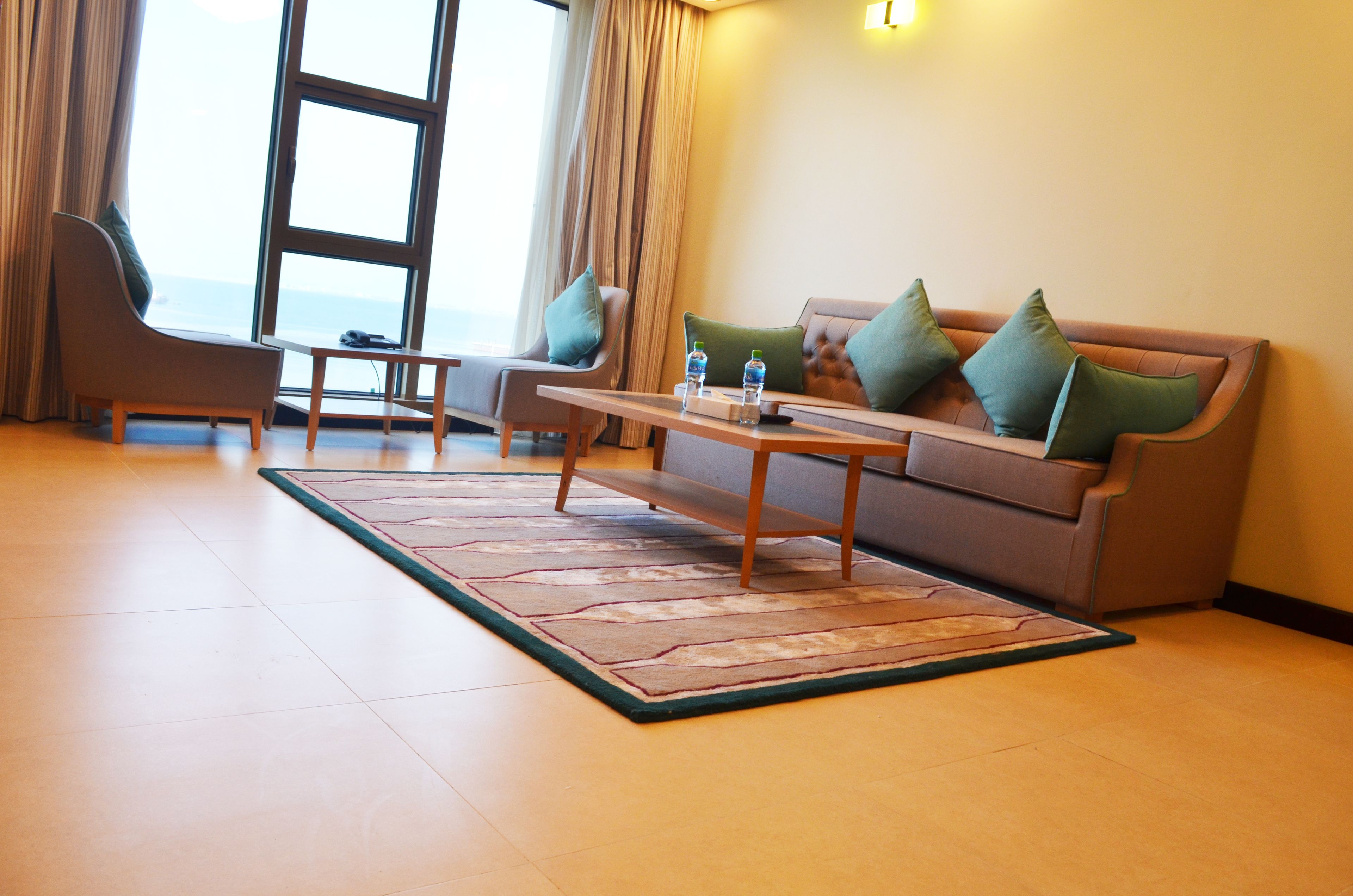 Una sala de estar moderna con sofá, sillón y mesa de centro, un ventanal con cortinas y vistas al océano.