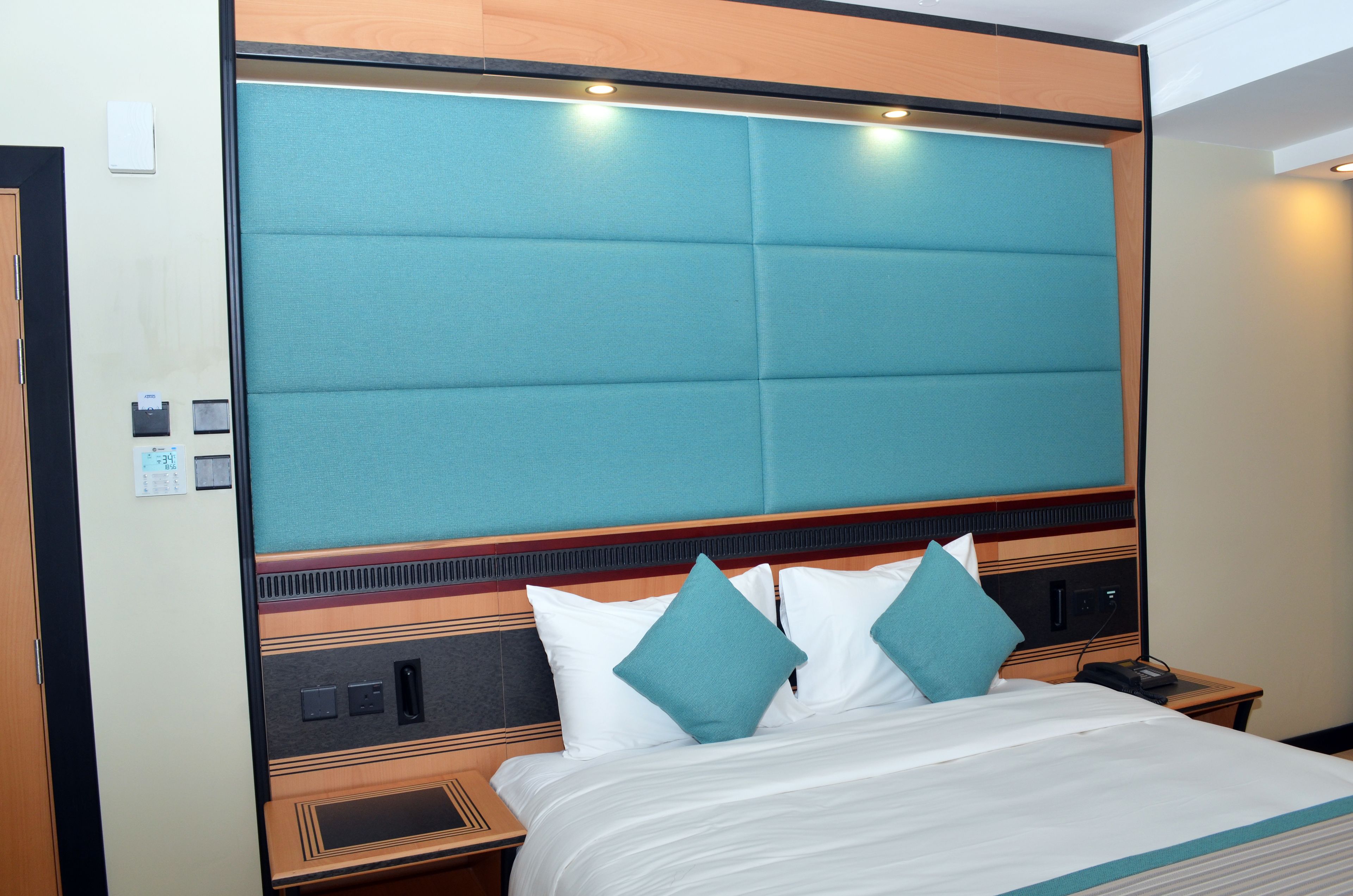 Una habitación de hotel con una cama grande, un cabecero con panel color turquesa y un detalle de madera.
