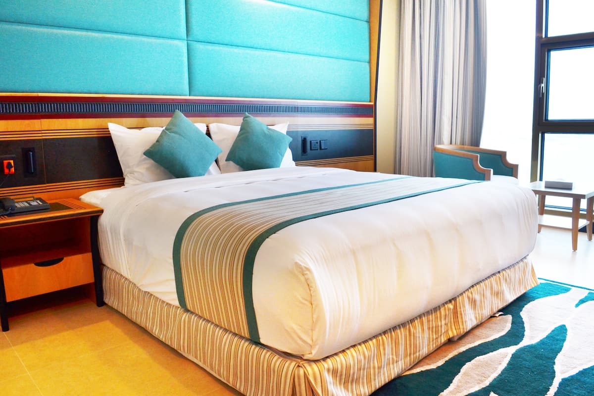 A hotel room with a large bed, a wooden nightstand, a desk, and a chair.