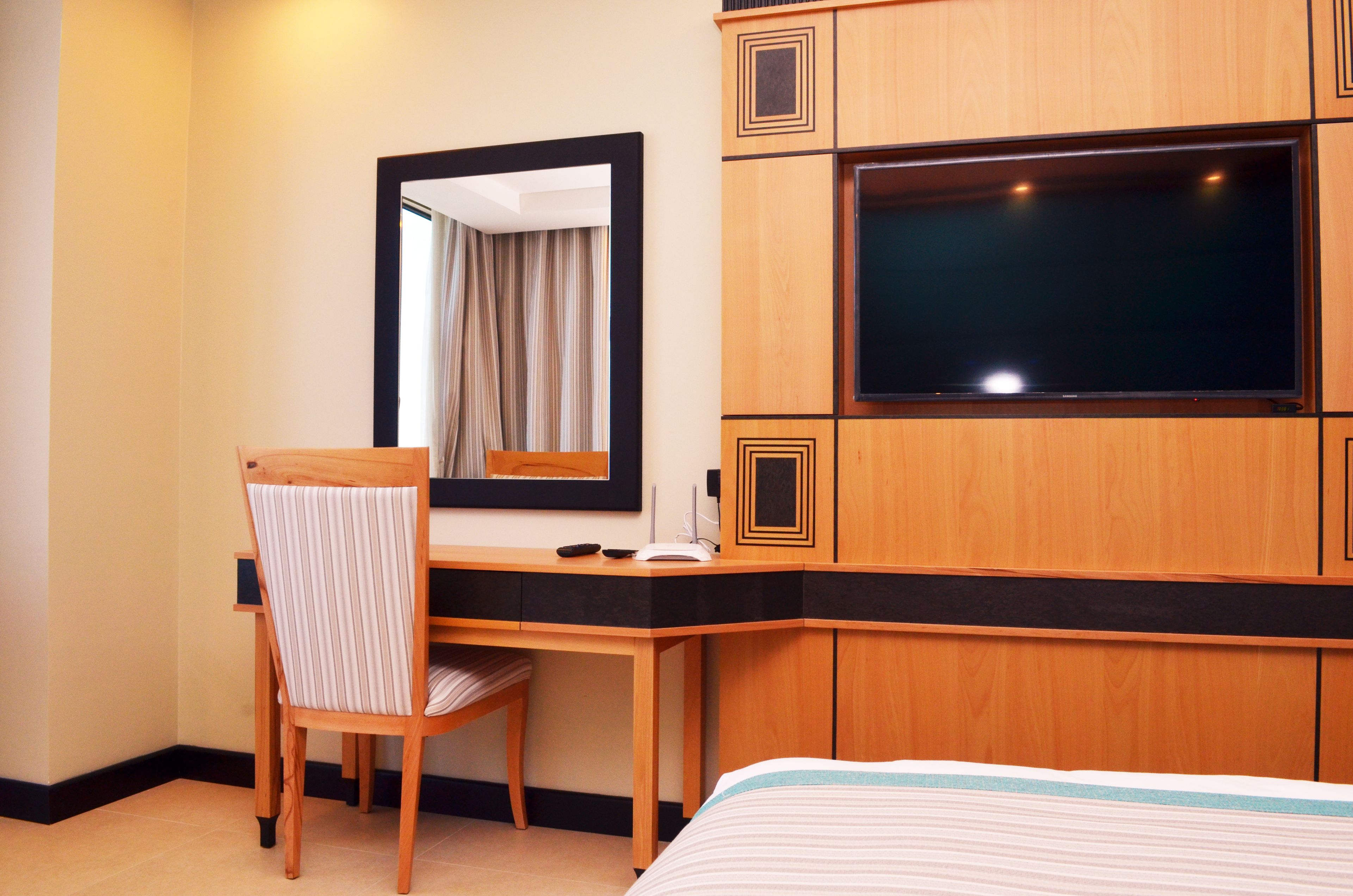 Ein Hotelzimmer mit einem Holztisch, einem Stuhl, einem Bett, einem Fernseher und einem Spiegel.