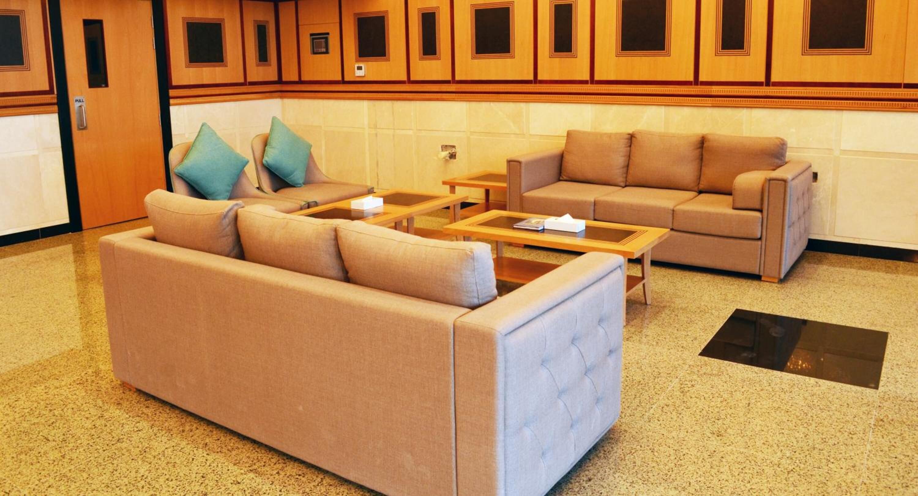 A hotel lobby with a large beige sofa, a smaller sofa, two armchairs, a coffee table, and a reception desk.