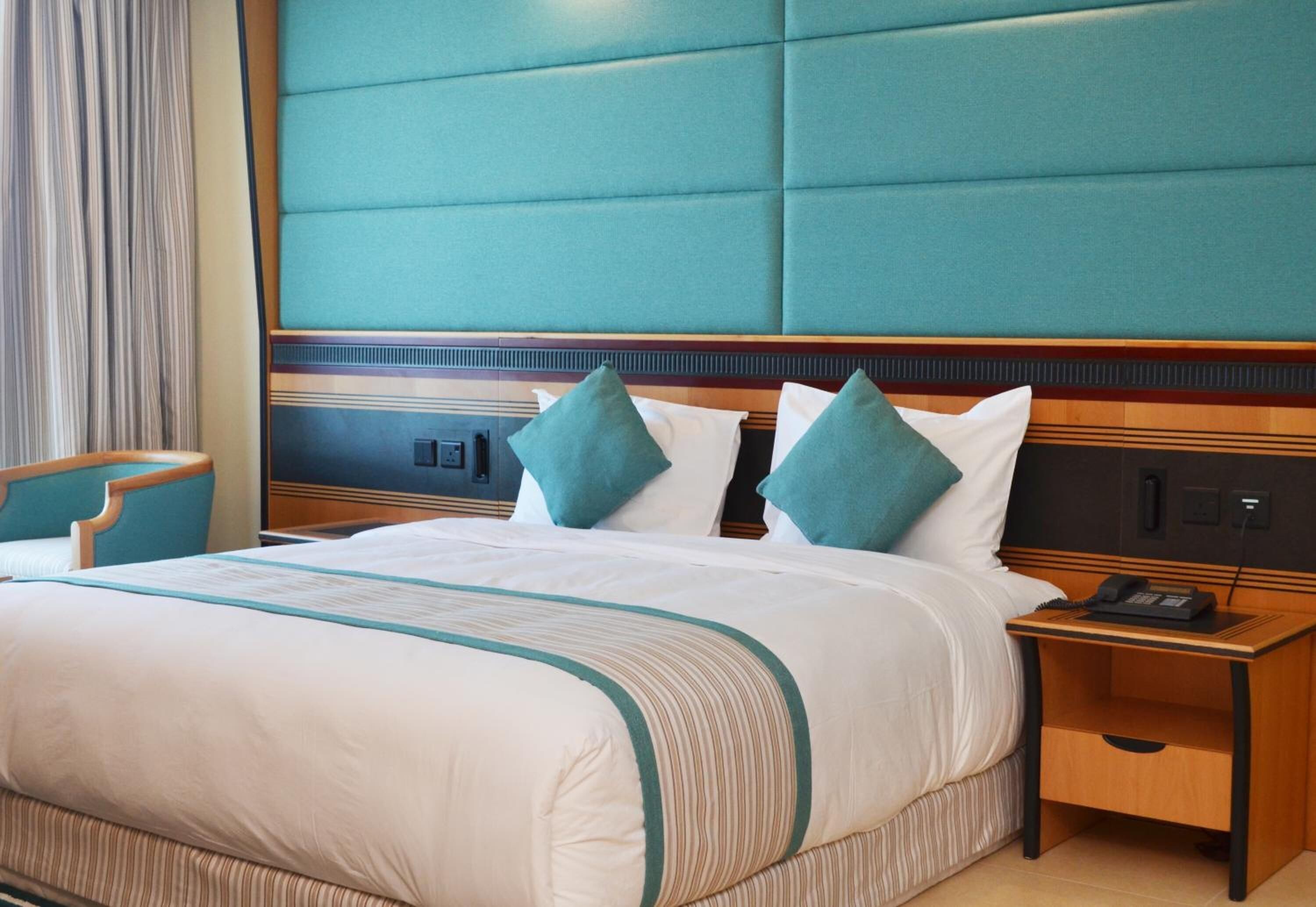 A hotel room with a large bed, a wooden nightstand with a telephone, and a chair.