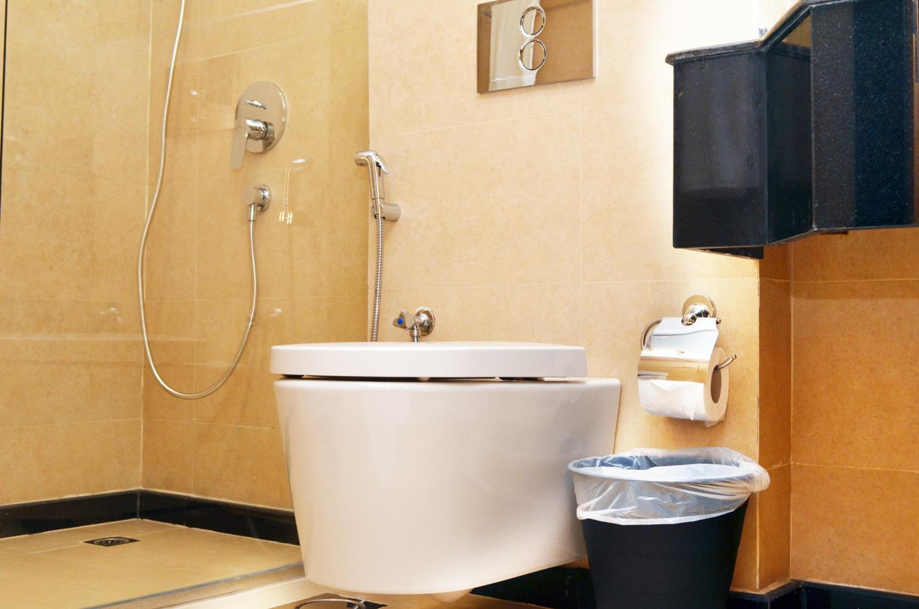 Un baño con inodoro blanco, ducha y un cubo de basura.