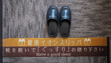 A pair of black slippers on a textured brown and gray carpet with a brown strip featuring Japanese text and English translation.