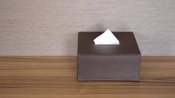 A small, dark brown, textured box with a white tissue on top, placed on a wooden surface against a plain wall.