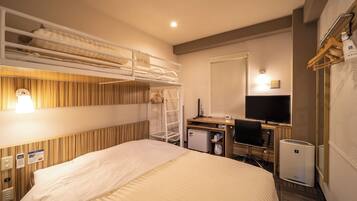 A hotel room with a bunk bed, a desk with a computer, a TV, and a minibar.