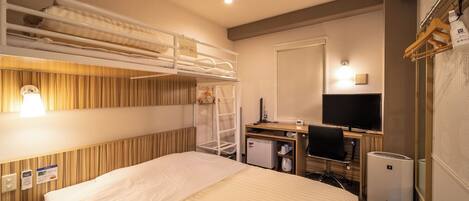 A hotel room with a bunk bed, a desk with a computer, a TV, and a minibar.