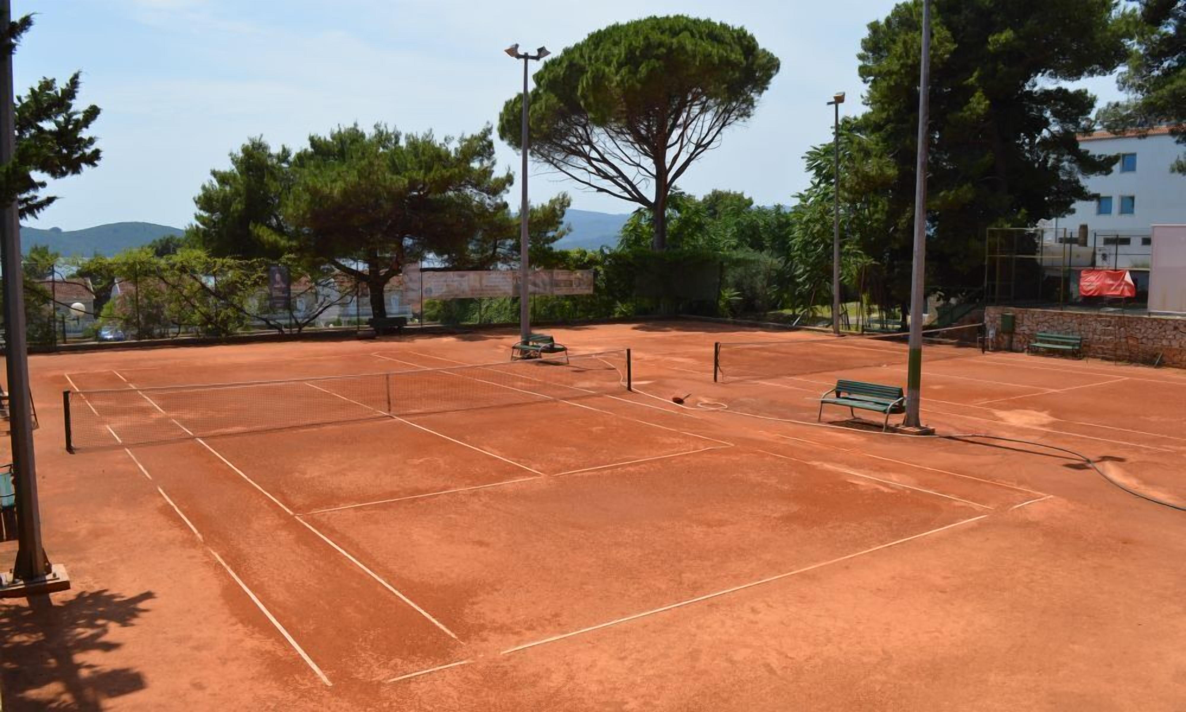 Ein Tennisplatz mit Bänken, Bäumen und einer Steinmauer.